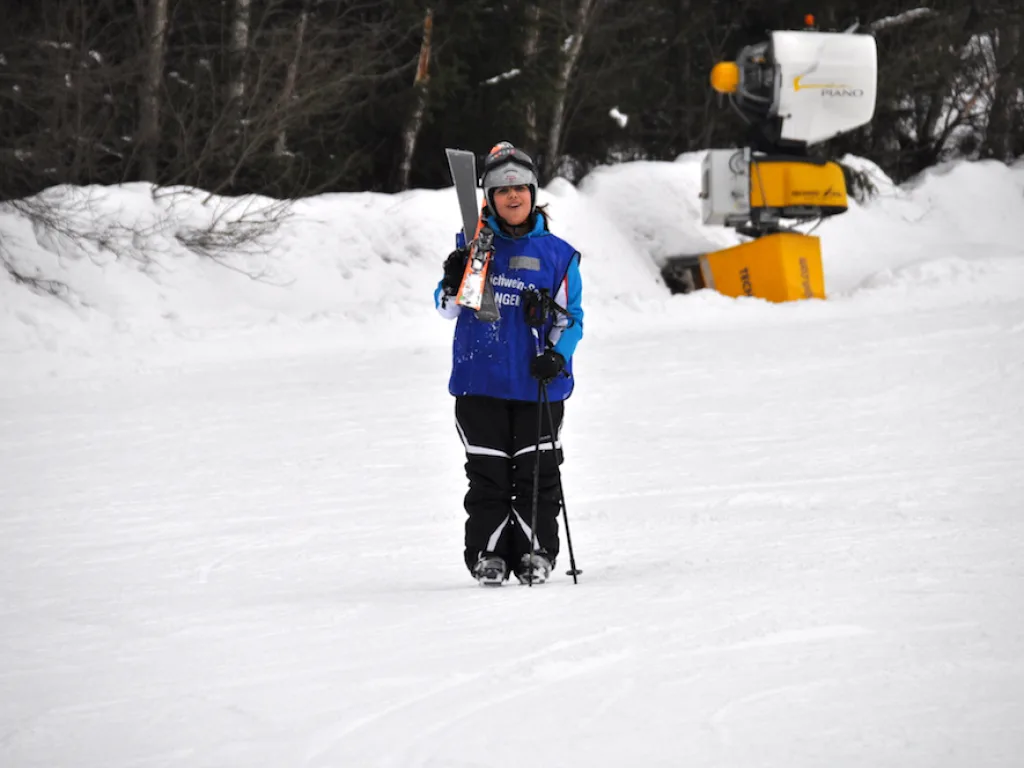 Person trägt die Ski geschultert über die Piste.